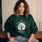 Dunkelgrünes Halloween-Sweatshirt mit mystischem Motiv: Eine brennende Kerze im Lineart-Stil vor einem großen Vollmond, darunter der Schriftzug ‚THE MIDNIGHT SOCIETY – telling tales, after dark‘. Design mit Retro- und Gruselflair.
