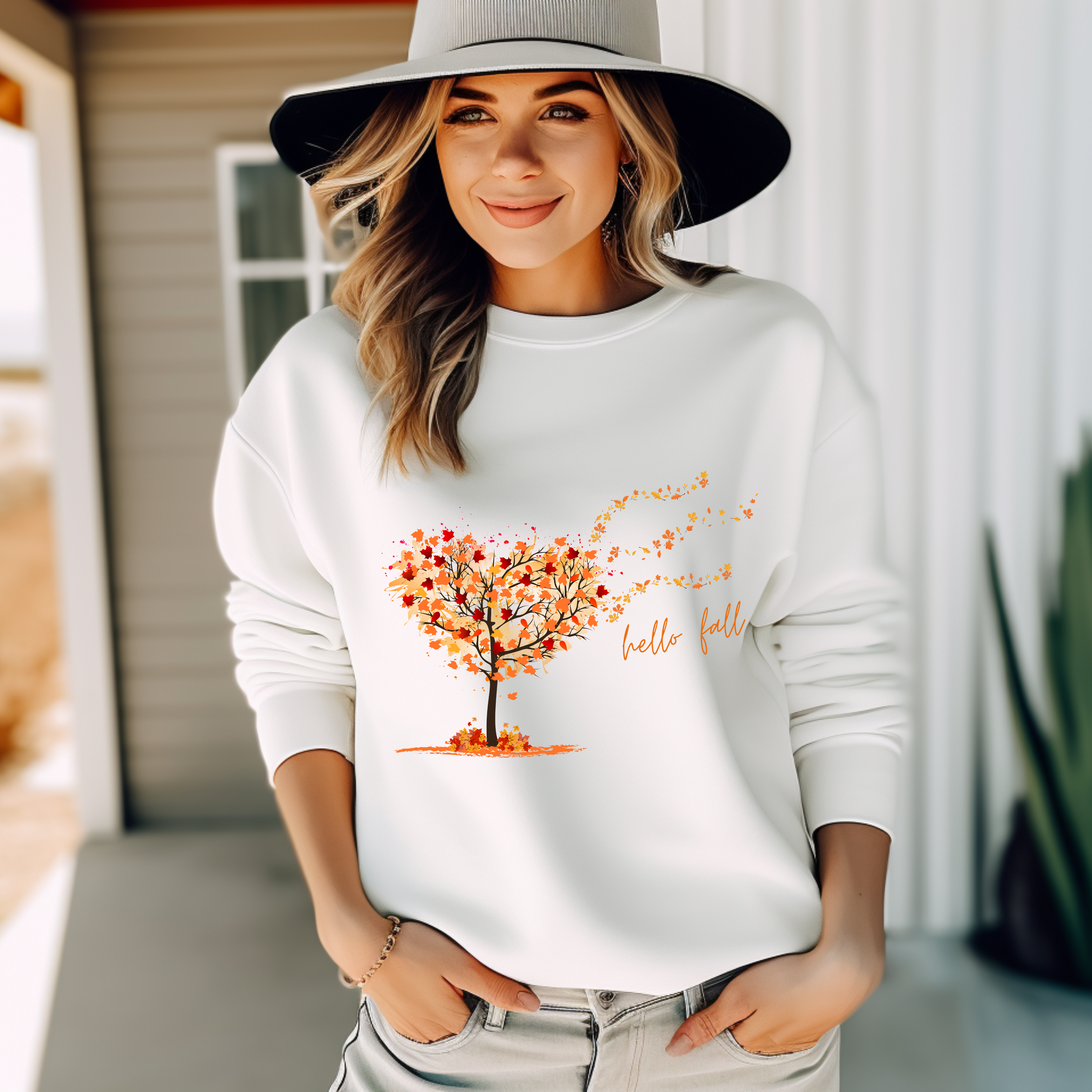 Sweatshirt mit Motiv eines geschwungenen Herbstbaums im Wind, dessen orange-, gelb- und rostrote Blätter durch die Luft wirbeln. Darunter handschriftlicher Schriftzug ‚hello fall‘. Romantisches, stimmungsvolles Herbstdesign
