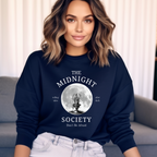Dunkelblaues Halloween-Sweatshirt mit mystischem Motiv: Eine brennende Kerze im Lineart-Stil vor einem großen Vollmond, darunter der Schriftzug ‚THE MIDNIGHT SOCIETY – telling tales, after dark‘. Design mit Retro- und Gruselflair.
