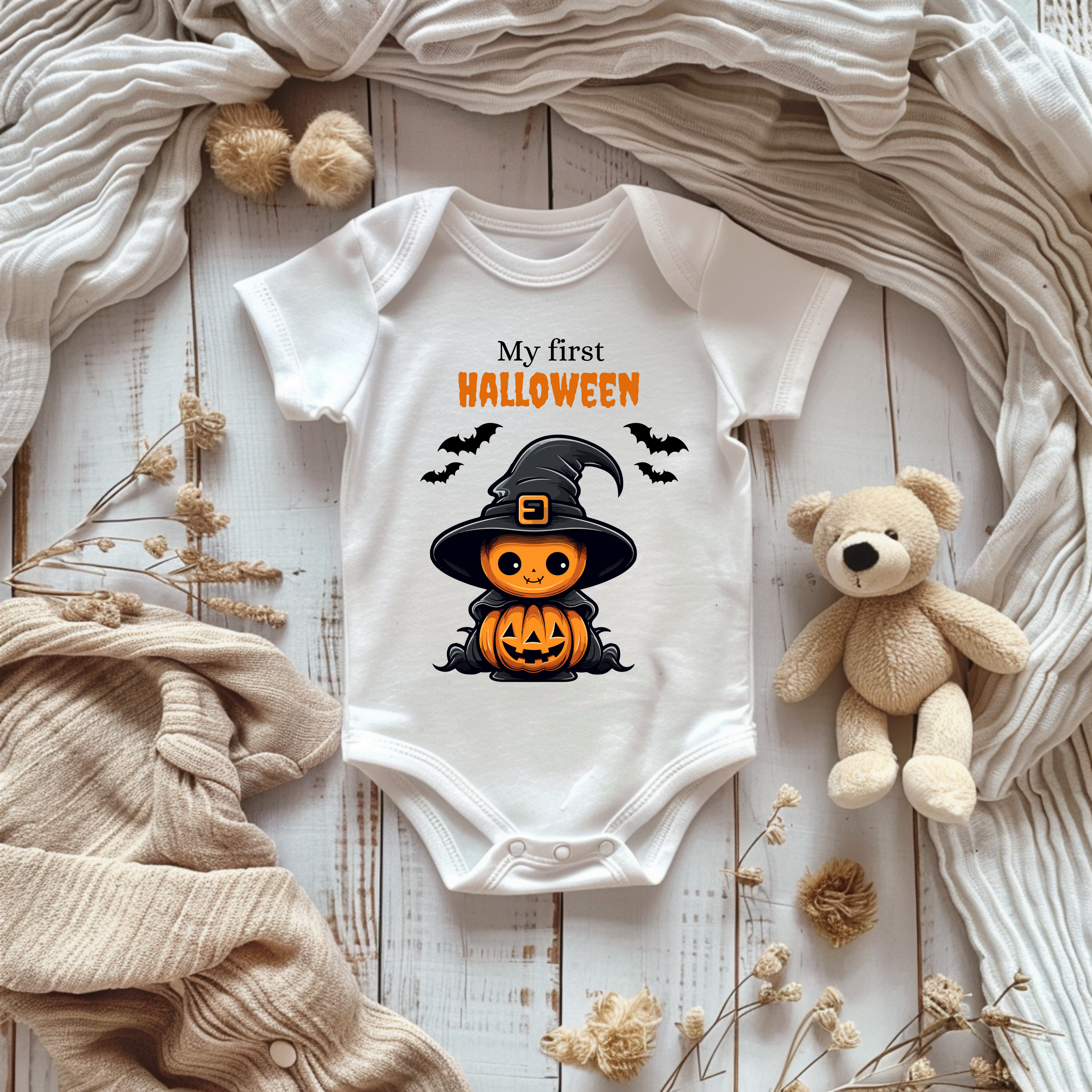 Weißer Kurzarm Baby-Strampler mit Halloween-Motiv: niedlicher Kürbis im Hexenkostüm mit Hut und Umhang, umgeben von Fledermäusen. Darüber der Schriftzug ‚My First Halloween‘.