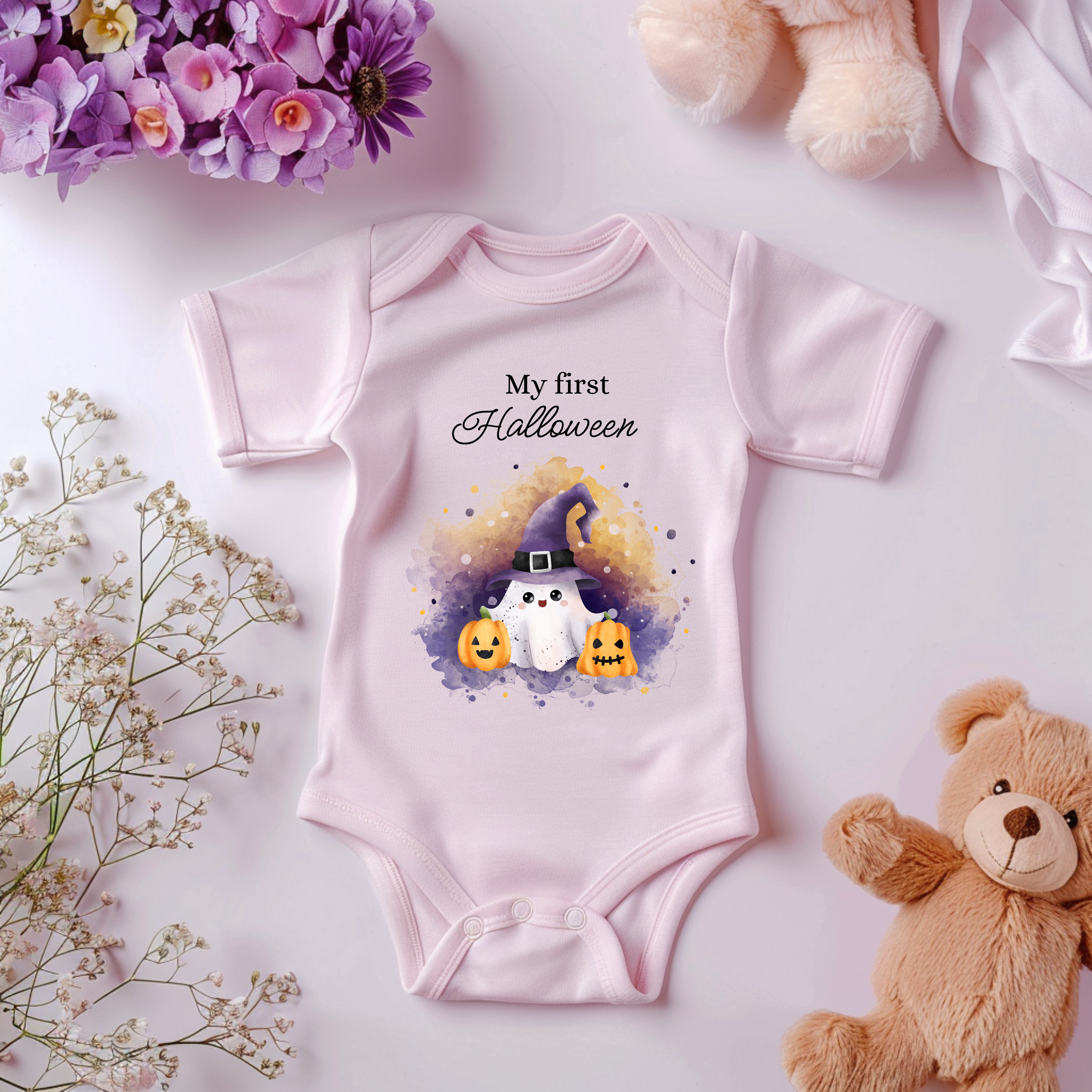 Rosa Baby-Strampler mit Halloween-Motiv: süßer kleiner Geist mit Hexenhut, umgeben von Kürbissen. Darüber der Schriftzug ‚My First Halloween‘ – perfekt für das erste Halloween.

