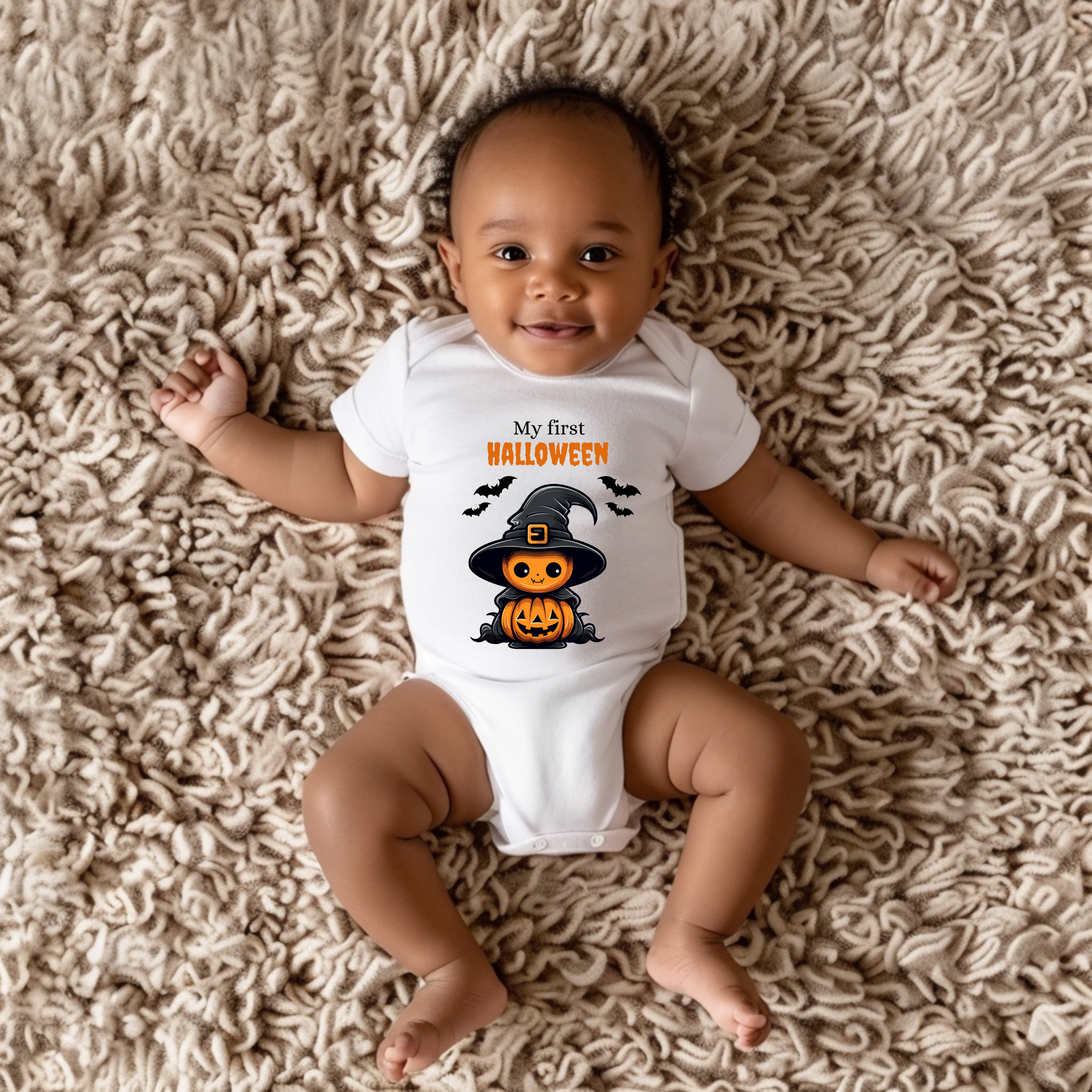 Weißer Kurzarm Baby-Strampler mit Halloween-Motiv: niedlicher Kürbis im Hexenkostüm mit Hut und Umhang, umgeben von Fledermäusen. Darüber der Schriftzug ‚My First Halloween‘.